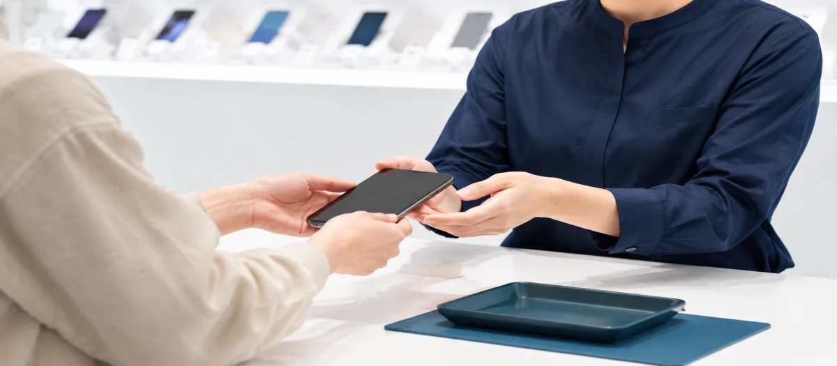 店舗スタッフにスマートフォンを渡す店頭買取のイメージ
